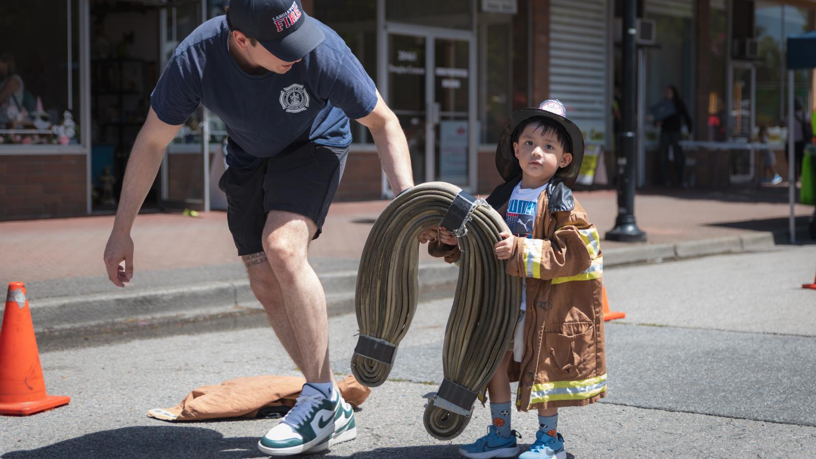 Little firefighter carrying hose at Community Day