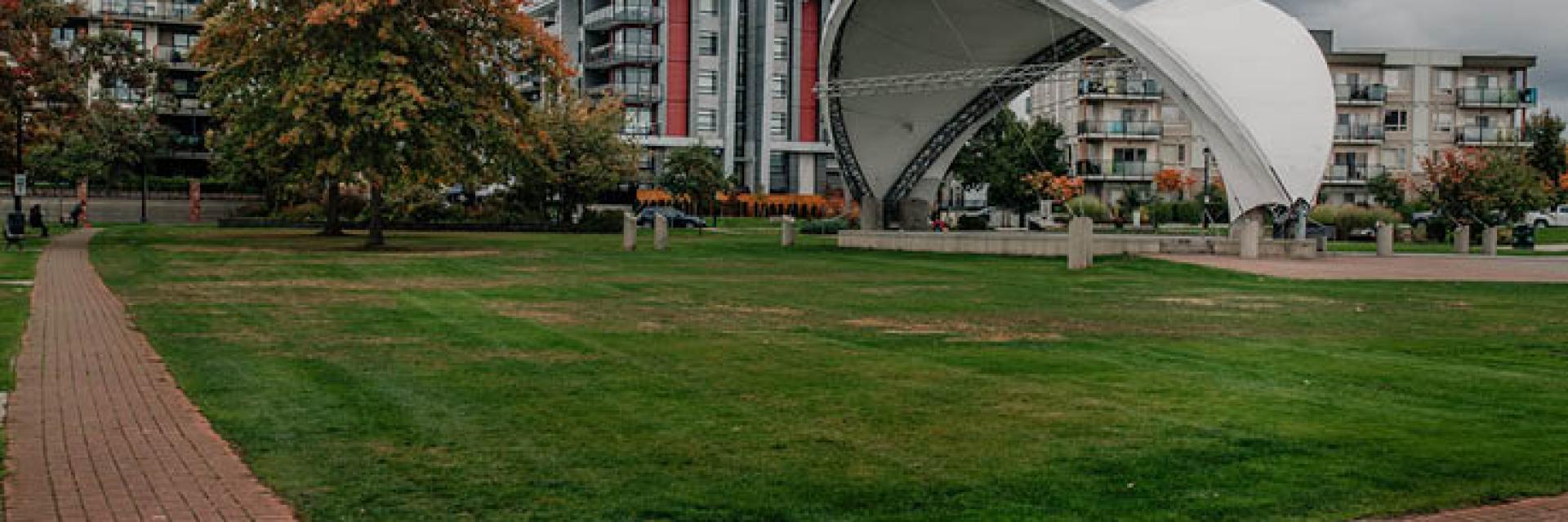 There is a stage with a modern-design roof in the background. The stage is surrounded by a brick-paved walkway.