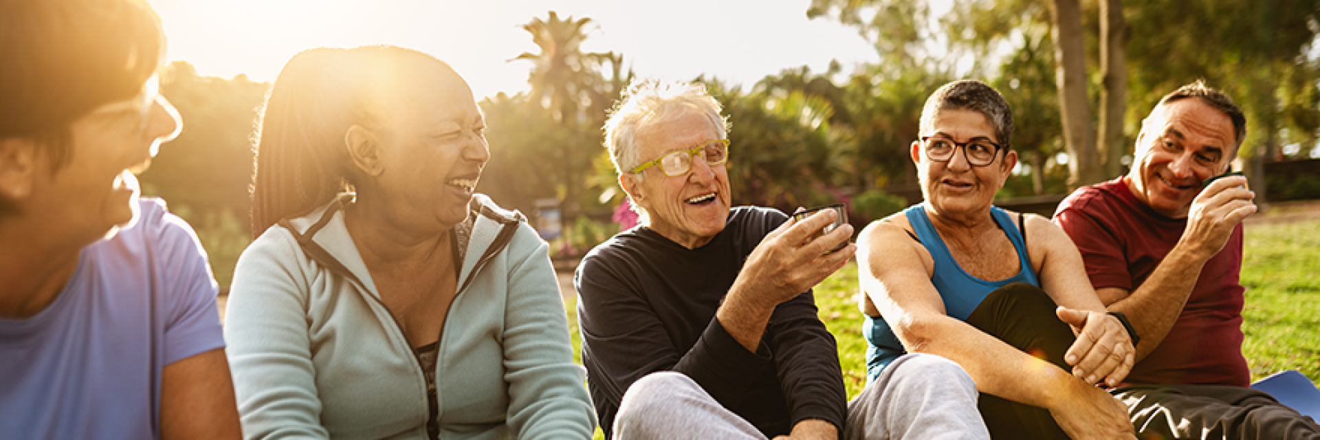Group of five seniors sitting outside in a parking laughing and talking after a fitness class.