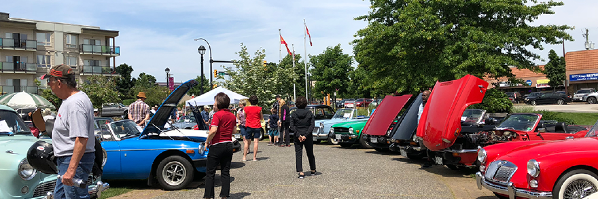 People walking through a park looking at vehicles that are in a car show.