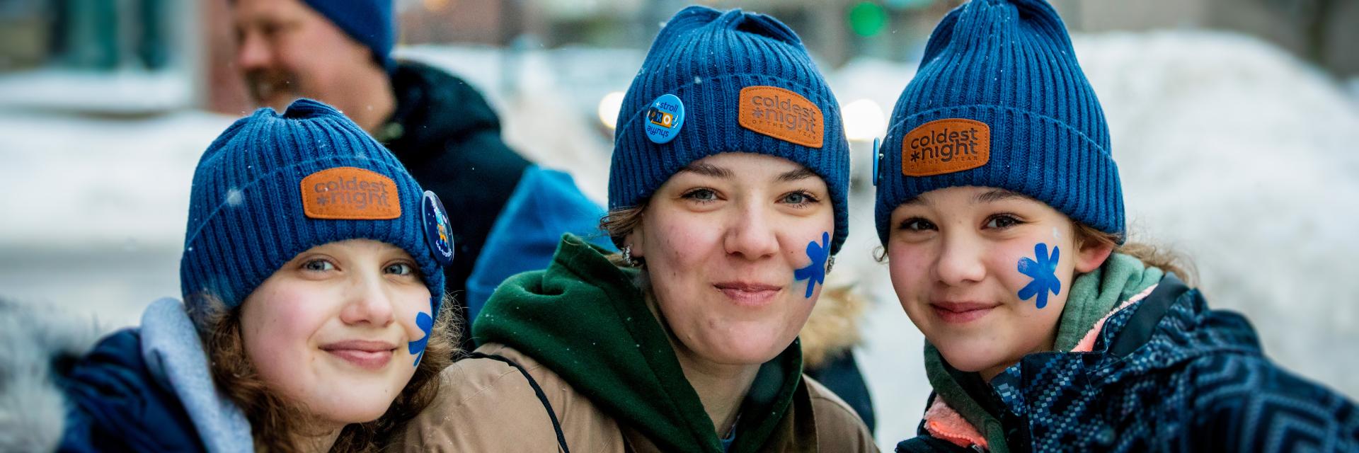 Three female participants of the Coldest Night of the Year fundraising walk standing outside, together, wearing toques and holding coffee.