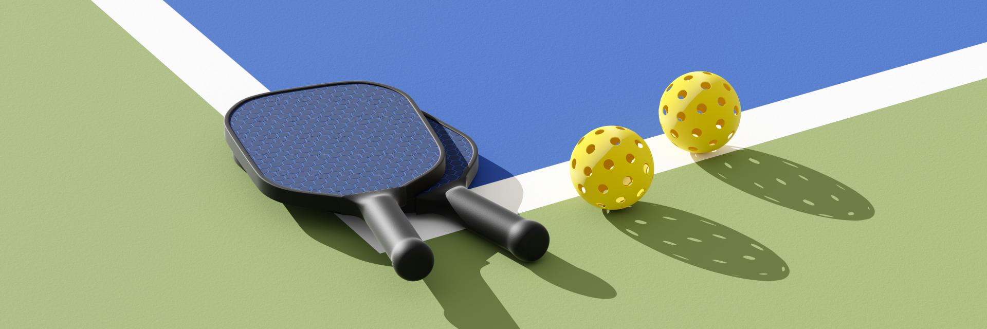 Two pickleball paddles and balls sitting on a court surface that is blue and green with a white line.