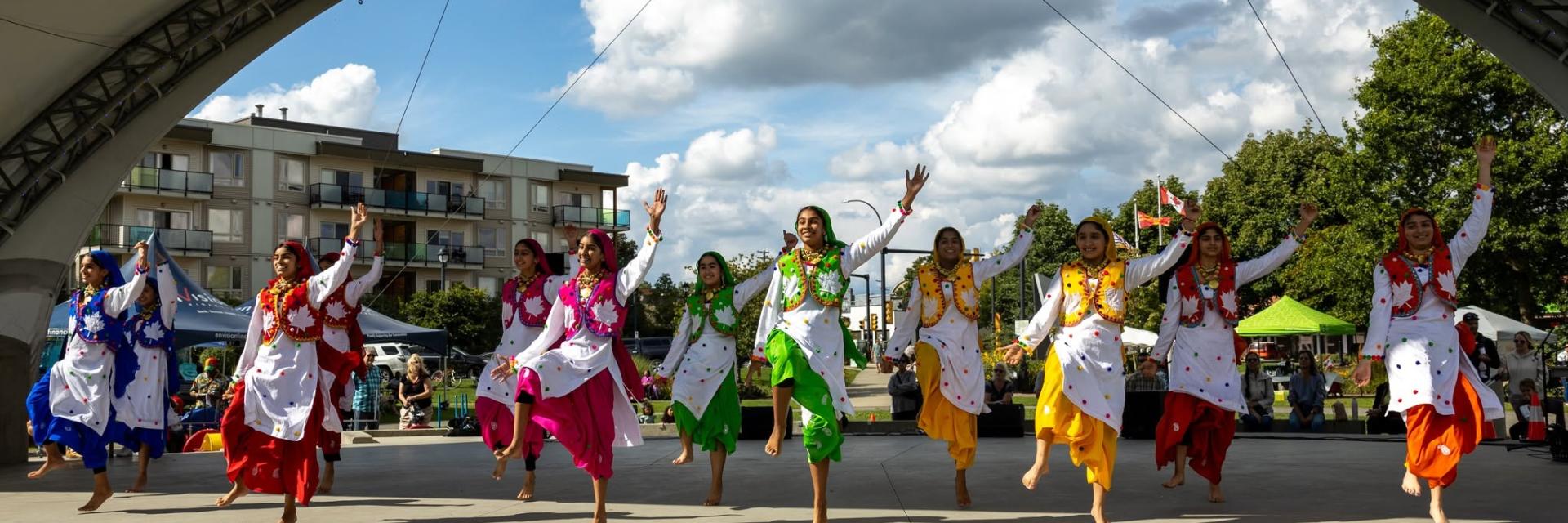 Several Bangura dancers wearing bright coloured outfits dancing on an outdoor stage.