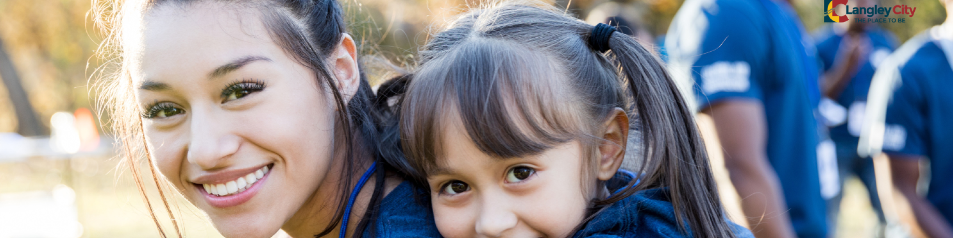 Woman and girl smiling. There is a group of people in the background.