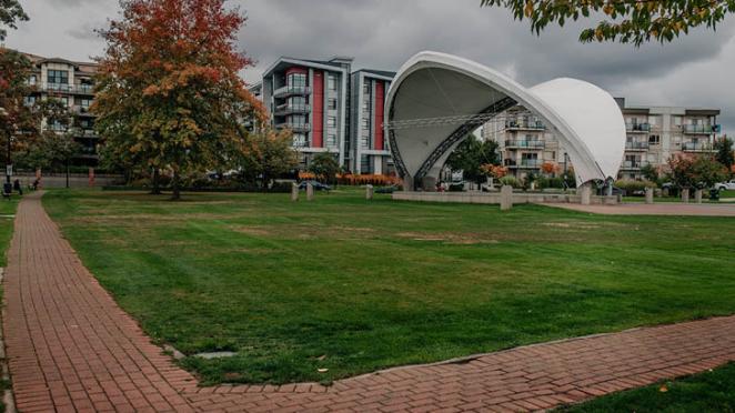 There is a stage with a modern-design roof in the background. The stage is surrounded by a brick-paved walkway.