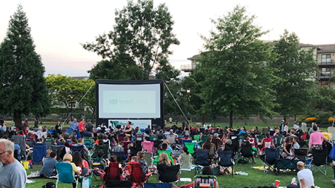 Crowd gather in park to watch a movie on a large inflatable screen.