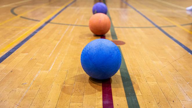 Gymnasium floor with a line of dodgeballs on the ground.