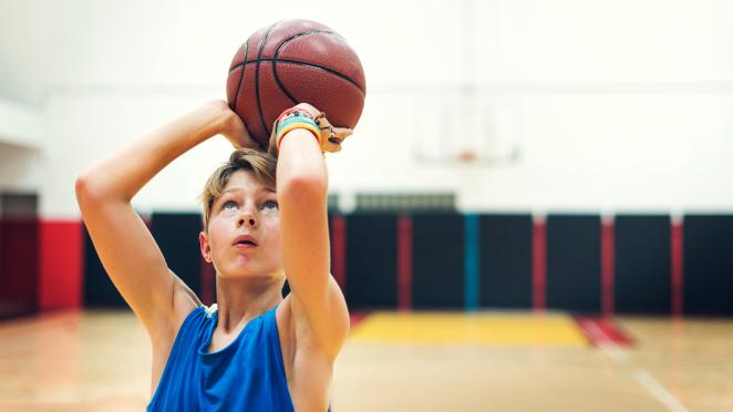 Teenage boy shooting a basketball inside a gymnasium.