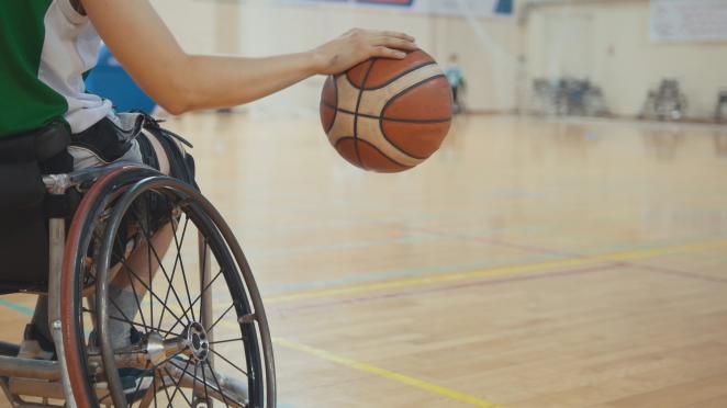 Individual in a wheelchair, dribbling a basketball inside a gymnasium.