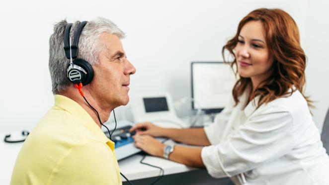 Senior taking part in a hearing test run by a technician.