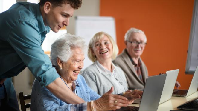 Three seniors sitting at computers getting help from an instructor.