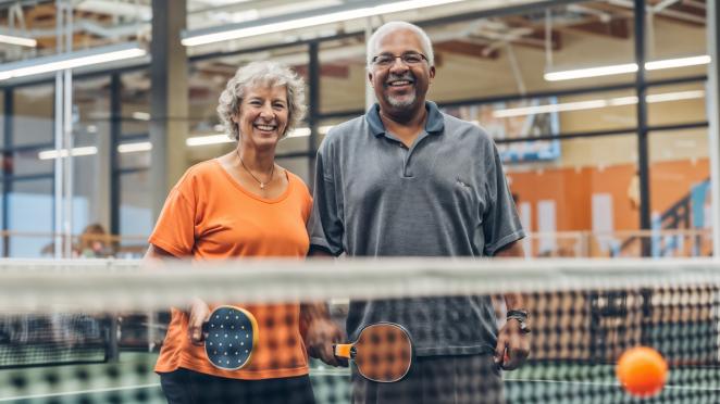 Two senior adults on a pickleball court holding paddles.