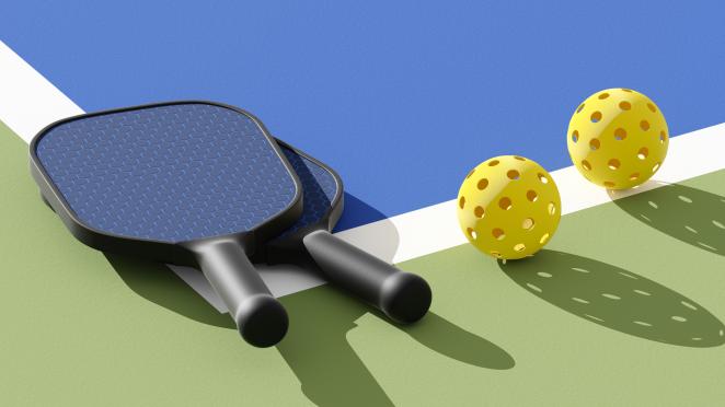 Two pickleball paddles and balls sitting on a court surface that is blue and green with a white line.