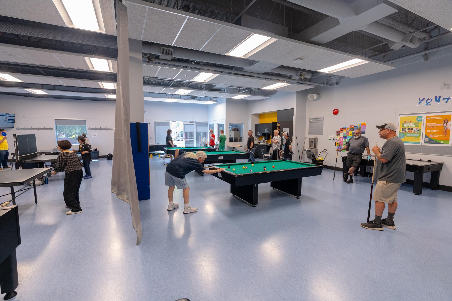 Several adults playing indoor pool and table tennis at a community centre.