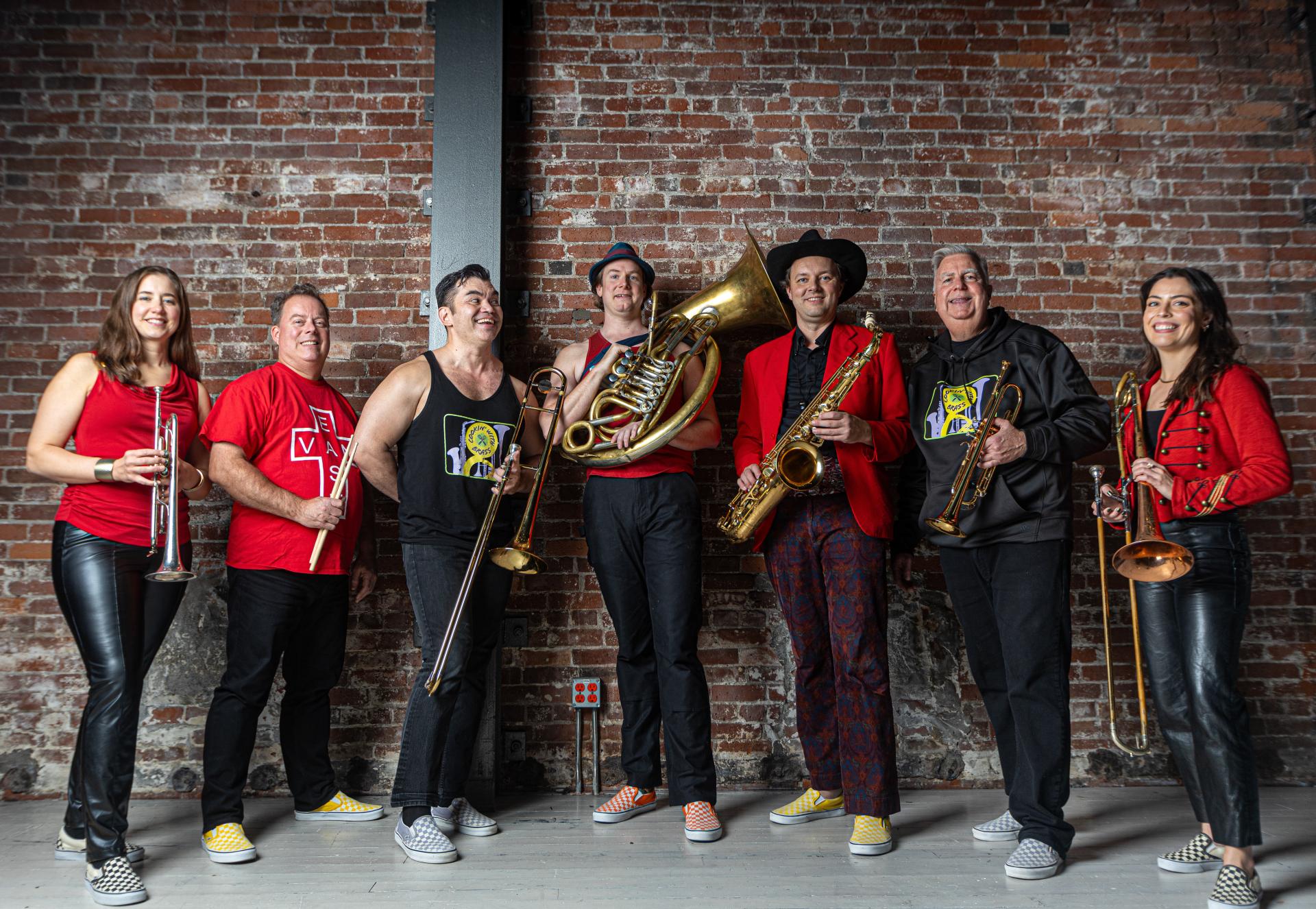 Seven people standing holding instruments against a brick wall.