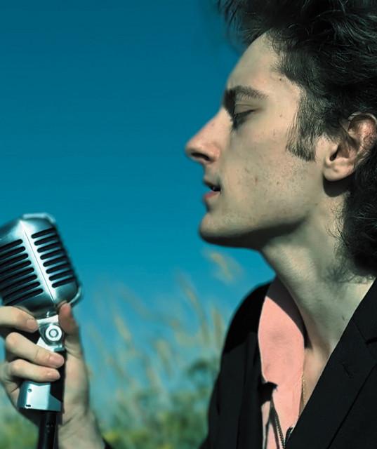 Single male singer standing next to microphone.