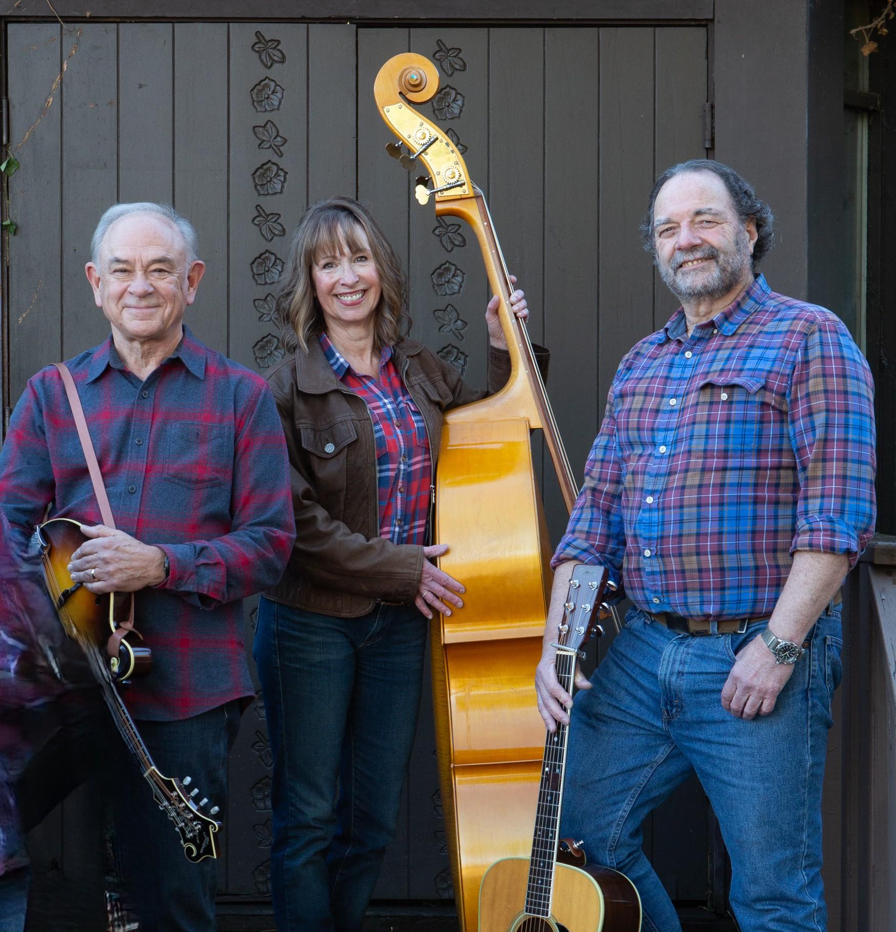 Three adults standing holding instruments, all wearing plaid blue and red t-shirts.